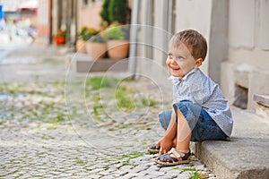 Little boy sits on the doorstep on a city street