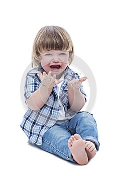 A little boy sits on the floor and cries. A child in jeans, a blue checkered shirt and a white T-shirt. Aggression and resentment