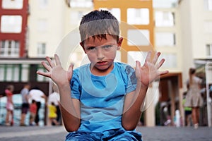 A little boy sits on the ground with his hands up and protests. The concept of raising a difficult naughty child.