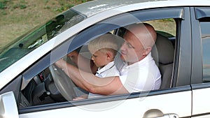 Little boy sits on the lap of his father driving a car, they learn to drive car.