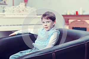 A little boy sits in a leather chair.