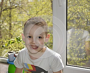 a little boy sits near the window, looks at the camera and smiles cheerfully