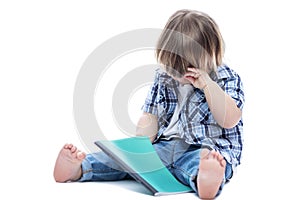 A little boy sits with a notebook and cries. A child in jeans and a blue checkered shirt. Training and education.  on a