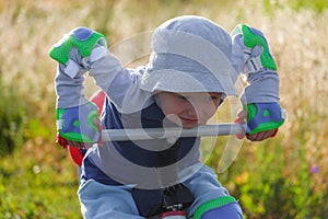 Little boy sits on a tricycle and holds hands behind the wheel