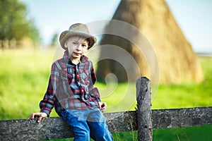 Little boy sits on wooden fence against picturesque haystack