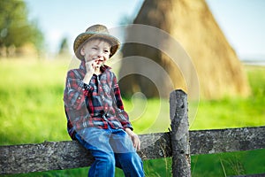 Little boy sits on wooden fence against picturesque haystack