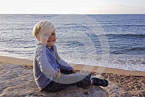 Little boy, sitting beach near sea, smiling