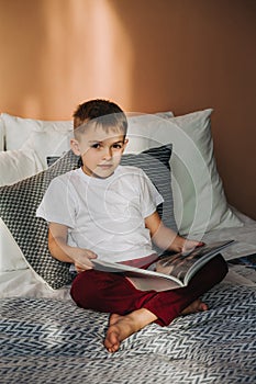 A little boy is sitting on the bed leafing through a magazine