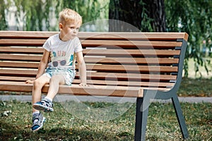 Little boy sitting on a bench. baby alone in the city