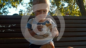 Little boy sitting on a bench and eating bun