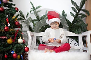 Little boy, sitting on a bench under christmas tree, eating choc