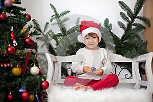 Little boy, sitting on a bench under christmas tree, eating choc