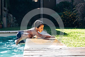 Little boy sitting in the border of swimming pool looking his mother into the pool