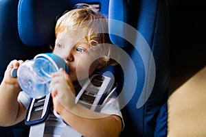 Little boy sitting in the car seat in the car, drinking.