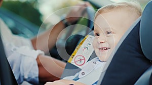 A little boy is sitting in a car seat near his father, smiling happily. Concept - safety and care