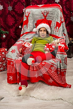 Little boy sitting on chair near Xmas tree