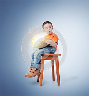 Little boy sitting on a chair with an open magic book, on blue background. Fairy tale concept