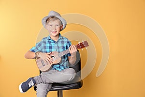 Little boy sitting on chair and playing guitar against color background