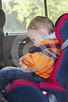 A little boy is sitting on a child& x27;s save seat in the car and fastens his seat belt himself