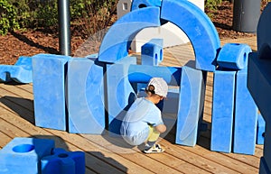 little boy is sitting on childrens playground in park with blue giant geometric figures for the development of imagination and