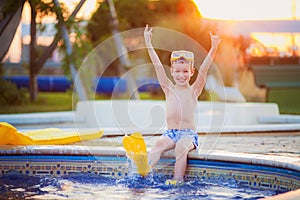 Little boy sitting on the edge of the pool and showing sign of the horns at the sunset