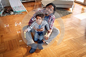 A little boy sitting in the father`s lap and making soap bubbles. Family, together, love, playtime