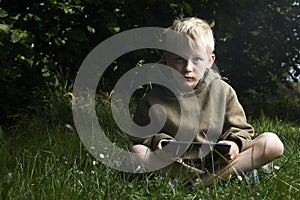 Little boy sitting on grass and using tablet computer