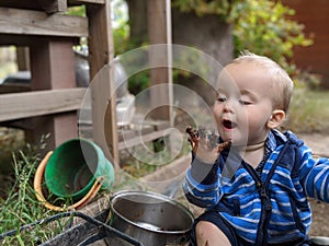 Little boy sitting on the ground looking at his muddy hand