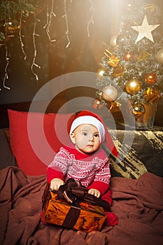 Little boy sitting and holding present in Santa Claus hat.