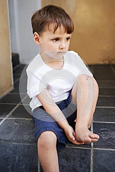 Little boy, sitting and injury on knee in home and accident, ache and with blood from cut. Young child, sad and holding