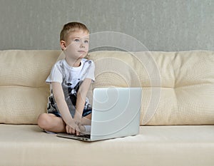 Little boy sitting with laptop on the couch at home