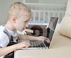 Little boy sitting with laptop on the couch at home