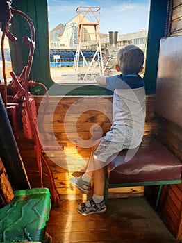 Little boy sitting on the machinist or train engineer seat in old steam locomotive and looking out of the window