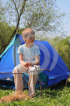 Little boy sitting near blue tent on nature photo