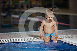 Little boy sitting poolside and dangling legs in water