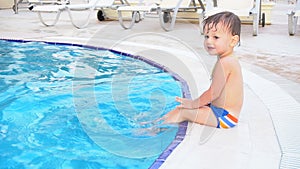 The little boy is sitting poolside at the resort