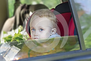 A little boy is sitting in a safety seat and looking out the open car window