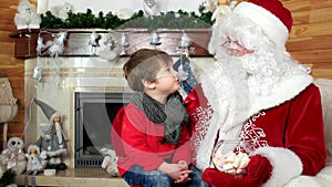 Little boy sitting on santa`s lap, child visiting santa claus winter residence and tell his wishes