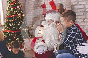 Little boy sitting in Santas lap whispering wishes for Christmas presents photo