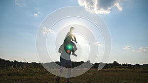 Little boy sitting on the shoulders of his dad and playing raised hands as airplane. Silhouettes of father and son