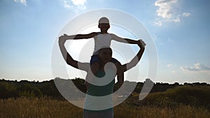 Little boy sitting on shoulders of his daddy and playing raised hands as airplane at sunset. Happy father and son