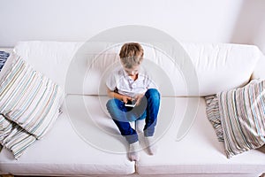 Little boy sitting on sofa, playing with smartphone