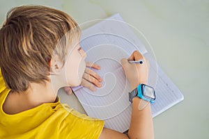 Little boy sitting at the table and looking smart watch. Smart watch for baby safety. The child makes school lessons
