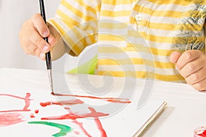 Little boy sitting at a table paints a picture of a white sheet