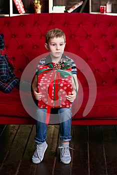 Little boy sitting with the teddy bear on the red coach with christmas present