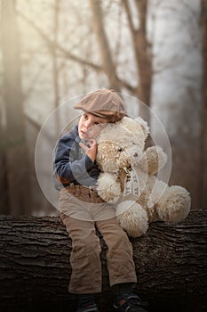 Little boy sitting on a tree and hugging a teddy