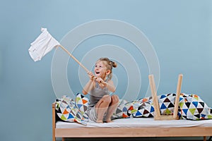 Little boy is sitting on unmade bed, waving white flag over blue walls