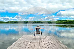 Little boy sitting on white empty deck chair at the lake dock.