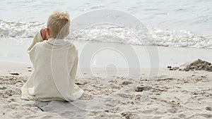 Little boy sitting wrapped in towel on ocean shore beach after swimming in sea. Summer vacation, holiday, family trip to