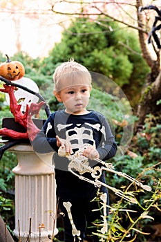 Little boy in a skeleton costume holding a skeleton on a halloween party